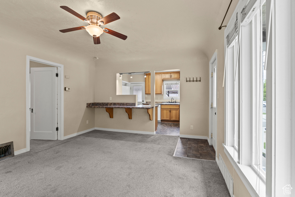 Kitchen featuring dark colored carpet, a kitchen bar, a ceiling fan, a peninsula, and baseboards