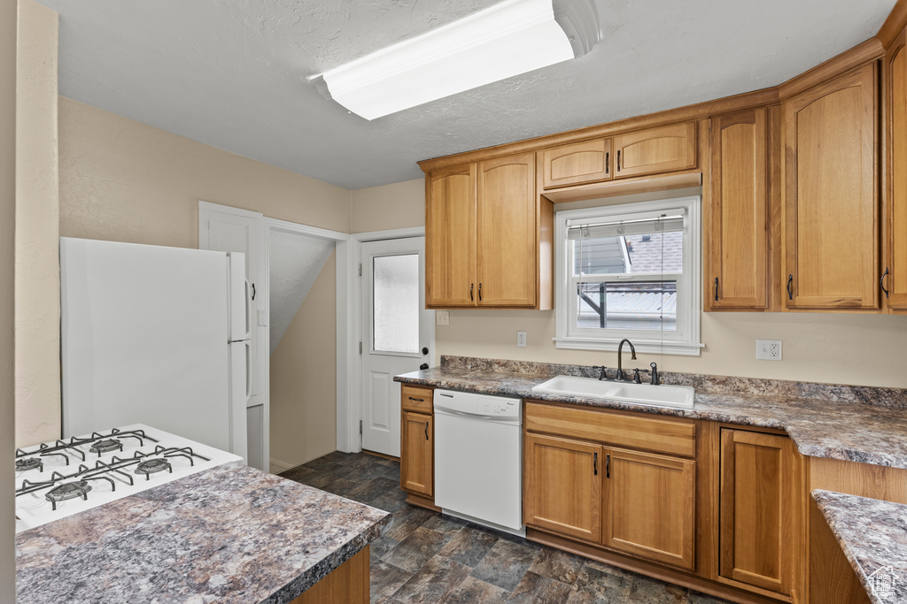 Kitchen featuring white appliances, a sink, stone finish flooring, and brown cabinets