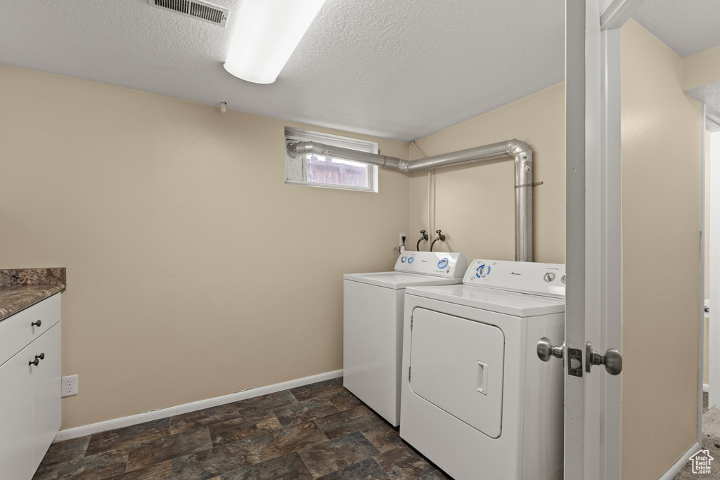 Laundry area with separate washer and dryer, baseboards, a textured ceiling, cabinet space, and dark stone finish floors