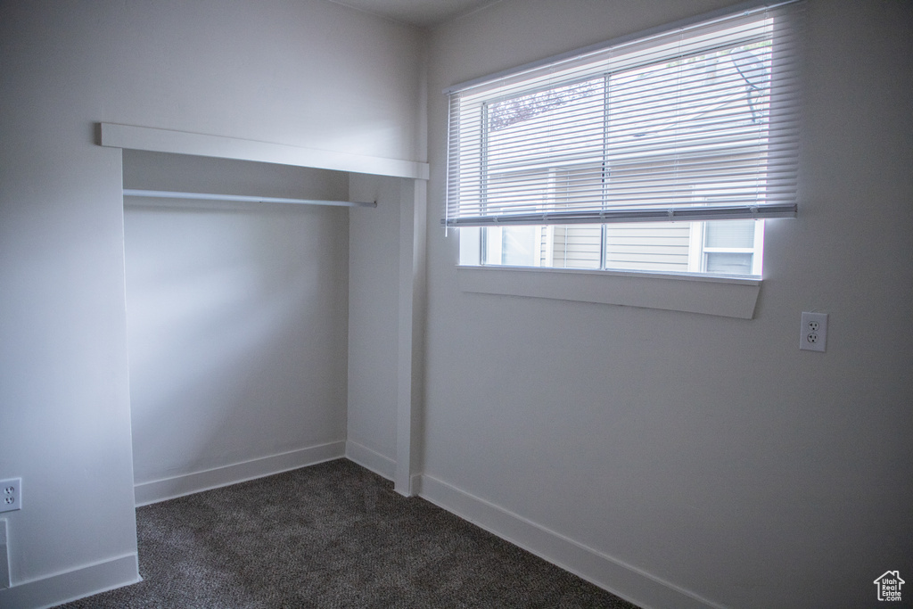 Unfurnished bedroom featuring dark carpet, a closet, and baseboards