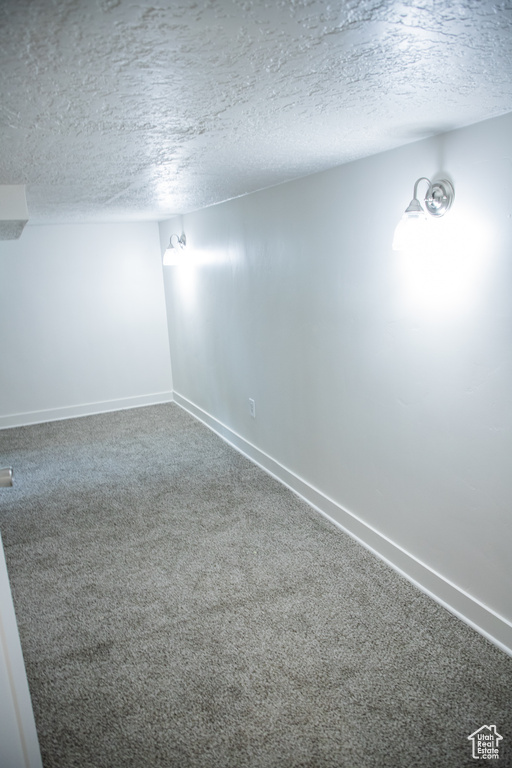 Carpeted spare room featuring a textured ceiling and baseboards