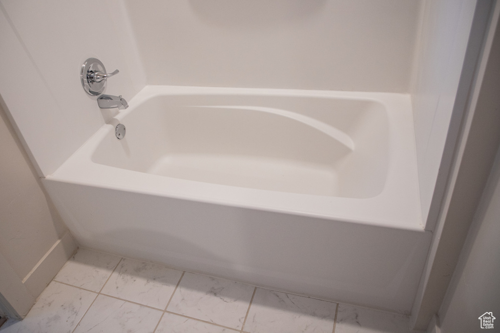 Full bath featuring marble look tiles and a tub