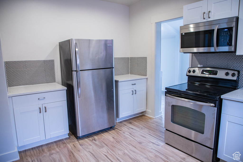Kitchen featuring stainless steel appliances, decorative backsplash, light wood-style floors, light countertops, and white cabinetry
