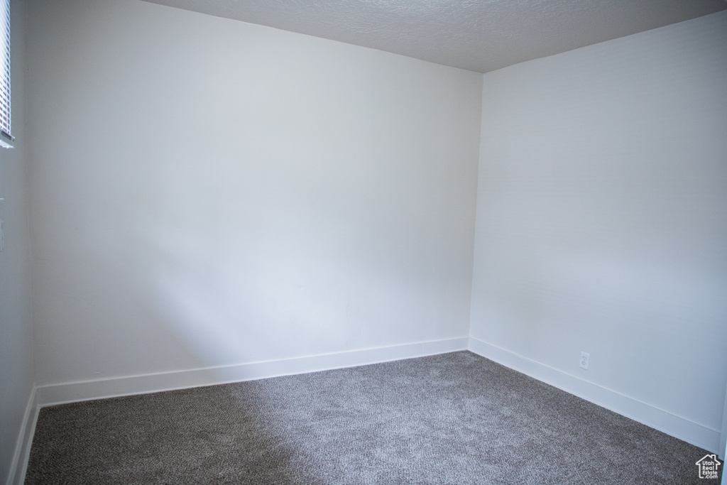 Empty room featuring dark carpet, baseboards, and a textured ceiling