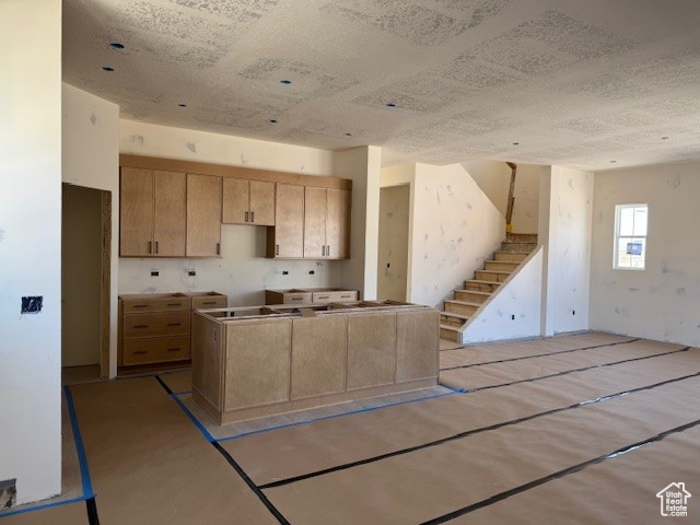 Kitchen featuring light brown cabinetry, a kitchen island, open floor plan, and a textured ceiling