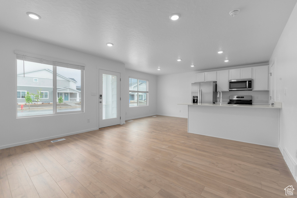 Kitchen featuring appliances with stainless steel finishes, white cabinetry, sink, light hardwood / wood-style floors, and kitchen peninsula