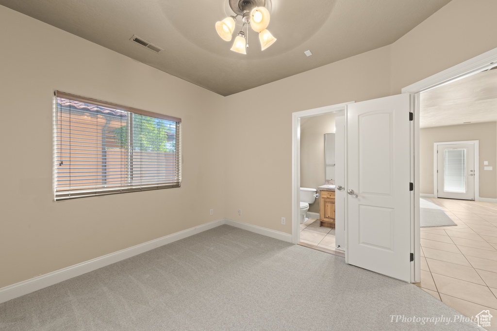 Unfurnished bedroom with ensuite bathroom, light tile patterned floors, and ceiling fan