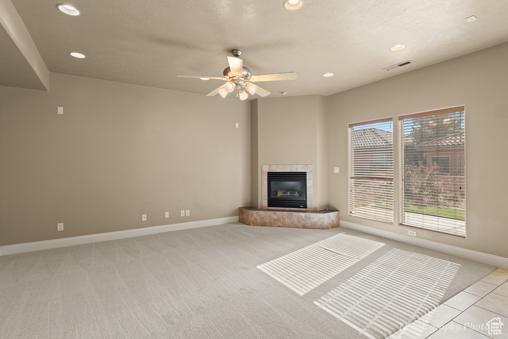 Unfurnished living room featuring a tiled fireplace and ceiling fan