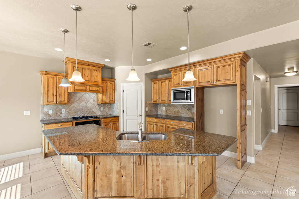 Kitchen featuring stainless steel microwave, a large island, light tile patterned floors, and backsplash