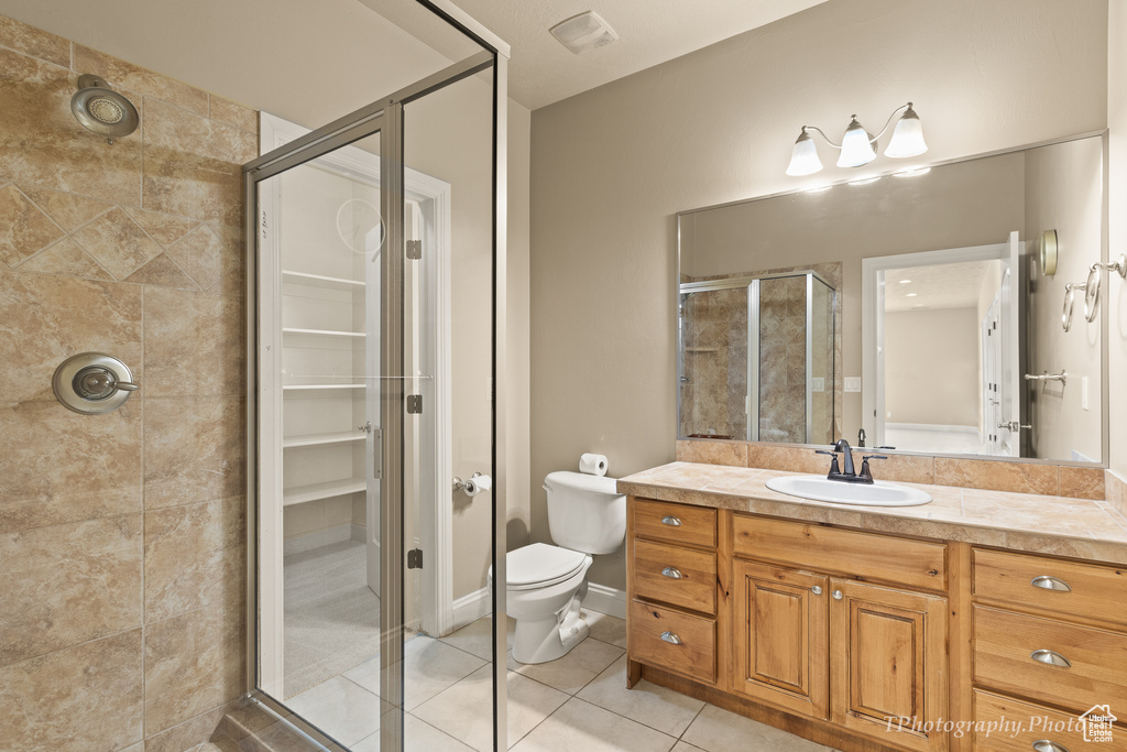 Bathroom featuring a shower with door, vanity, tile patterned floors, and toilet