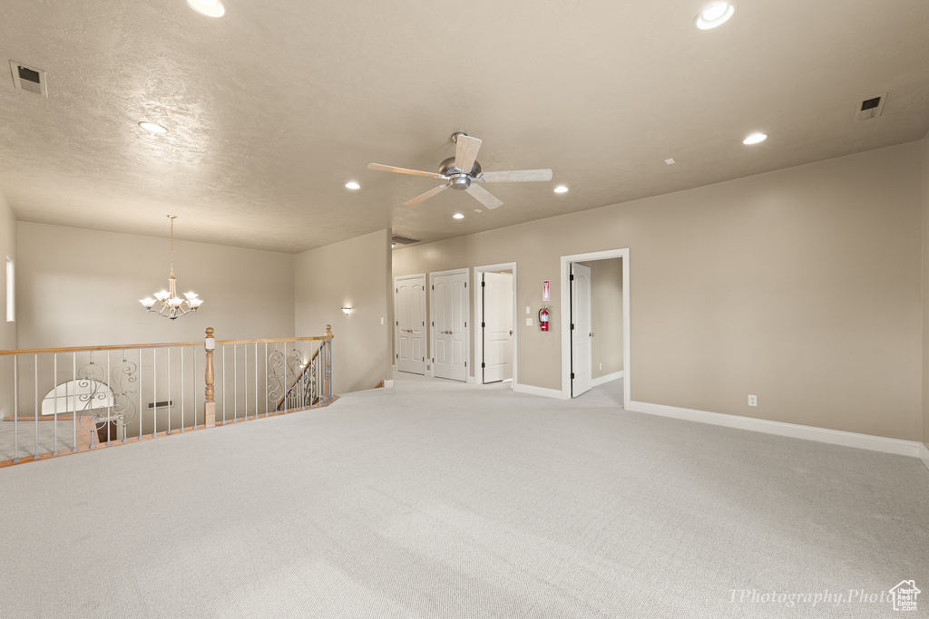 Carpeted spare room with ceiling fan with notable chandelier