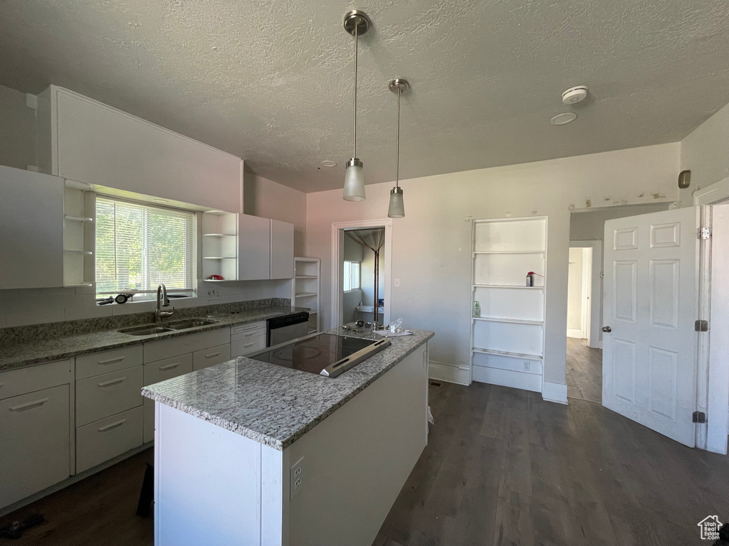 Kitchen with a sink, open shelves, black electric cooktop, a textured ceiling, and a kitchen island
