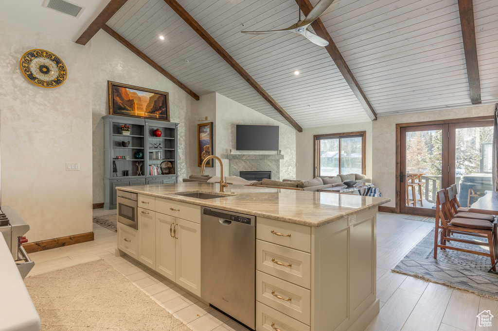 Kitchen with stainless steel dishwasher, a sink, ceiling fan, a center island with sink, and a large fireplace