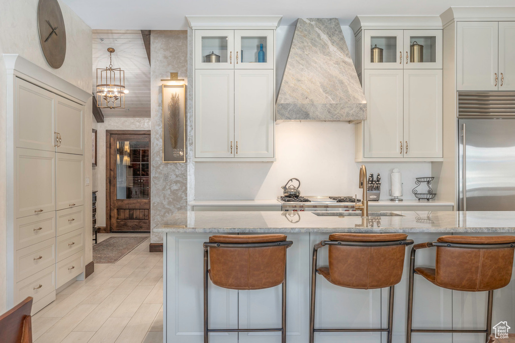 Kitchen featuring premium range hood, stainless steel built in refrigerator, a kitchen breakfast bar, and light stone countertops