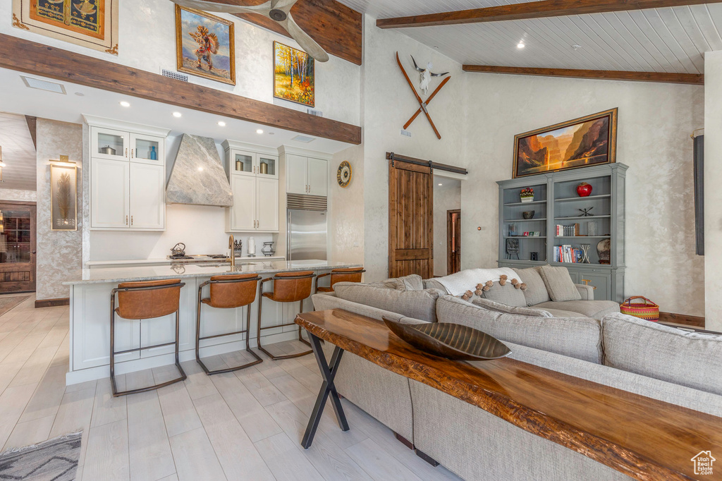 Living area with a barn door, high vaulted ceiling, light wood-style floors, and wood ceiling with exposed beams