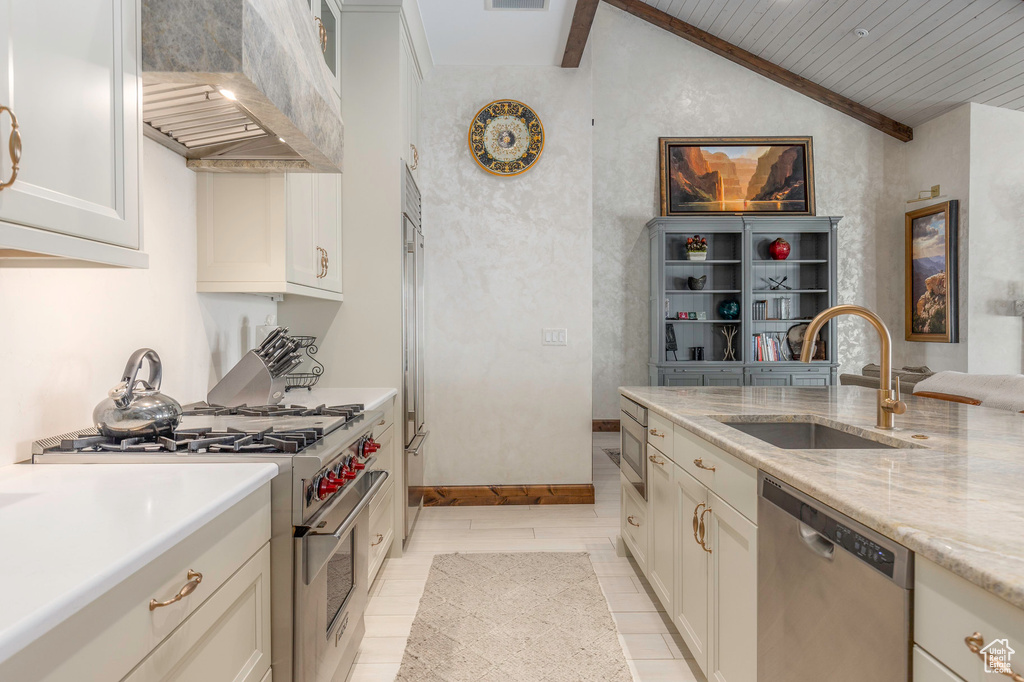Kitchen featuring high end appliances, a sink, wall chimney exhaust hood, white cabinets, and light stone counters