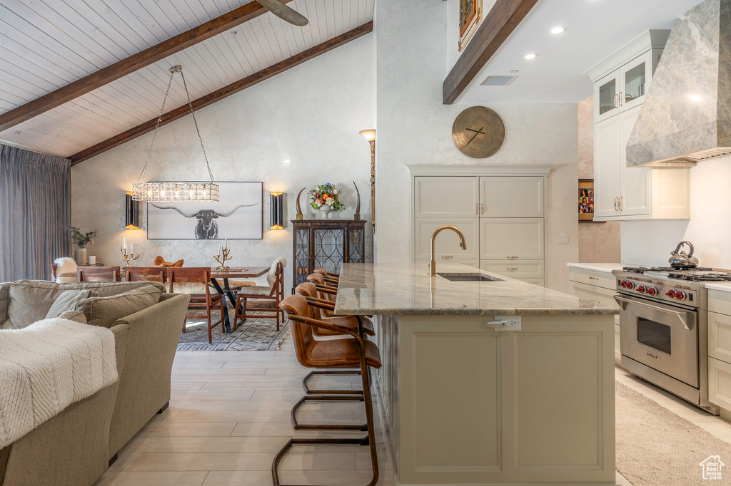 Kitchen featuring custom exhaust hood, premium range, a sink, light stone countertops, and wooden ceiling with exposed beams
