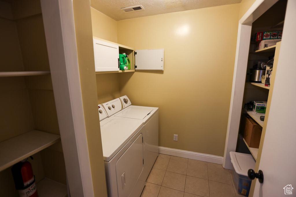 Washroom with cabinets, washer and dryer, and light tile patterned floors