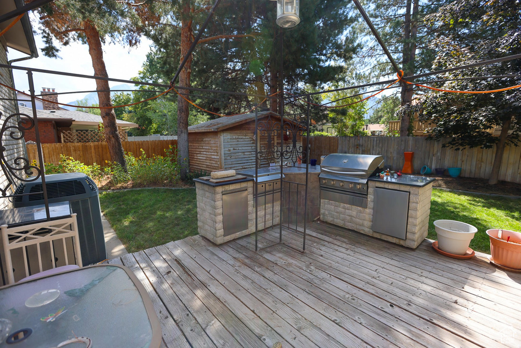 Wooden deck with a storage shed, grilling area, a yard, cooling unit, and exterior kitchen