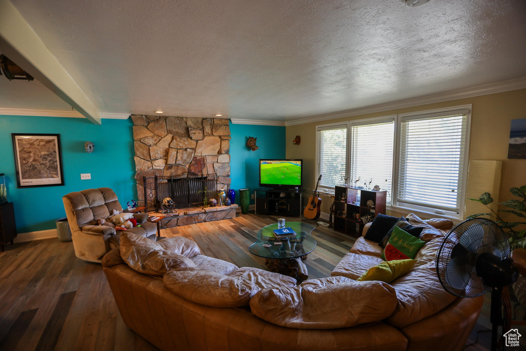 Living room with hardwood / wood-style flooring, ornamental molding, a stone fireplace, and a textured ceiling