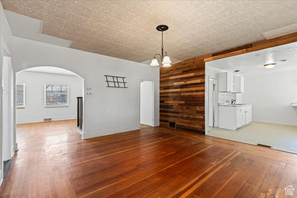 Unfurnished dining area featuring wood-type flooring, sink, an inviting chandelier, and wooden walls