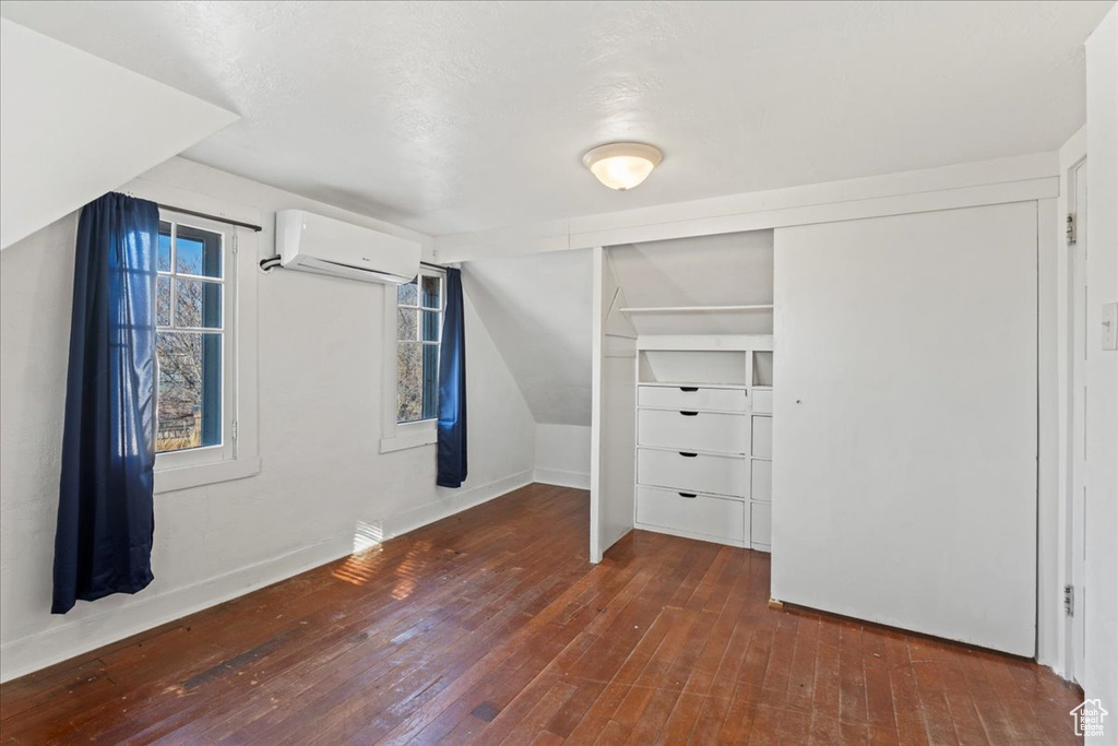 Unfurnished bedroom featuring an AC wall unit, dark wood-type flooring, lofted ceiling, and a closet