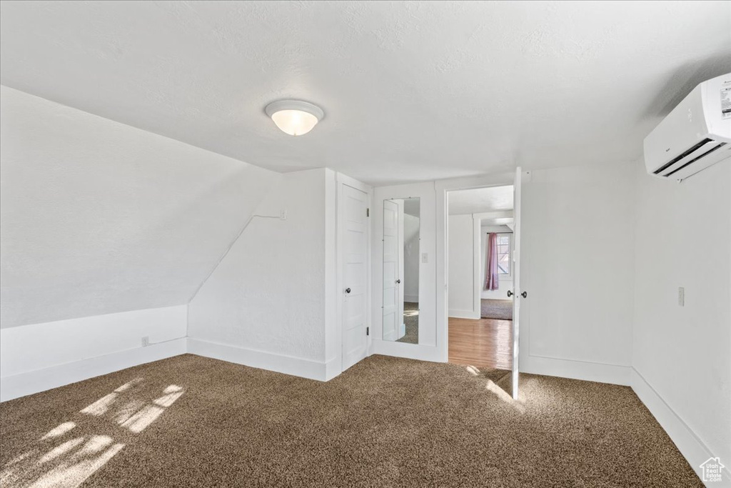 Additional living space featuring vaulted ceiling, carpet, and an AC wall unit