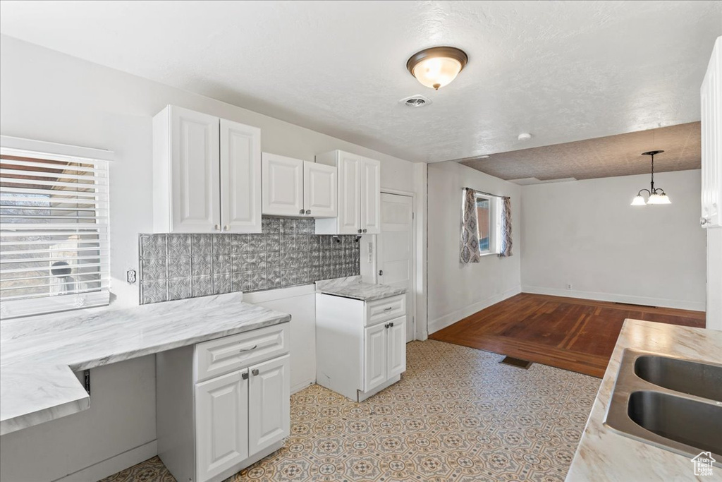 Kitchen featuring sink, decorative light fixtures, a notable chandelier, decorative backsplash, and white cabinets