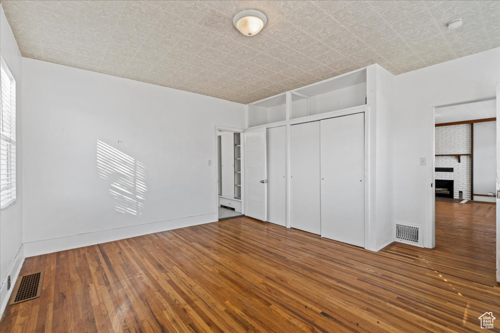 Unfurnished bedroom with a brick fireplace, dark wood-type flooring, and a closet