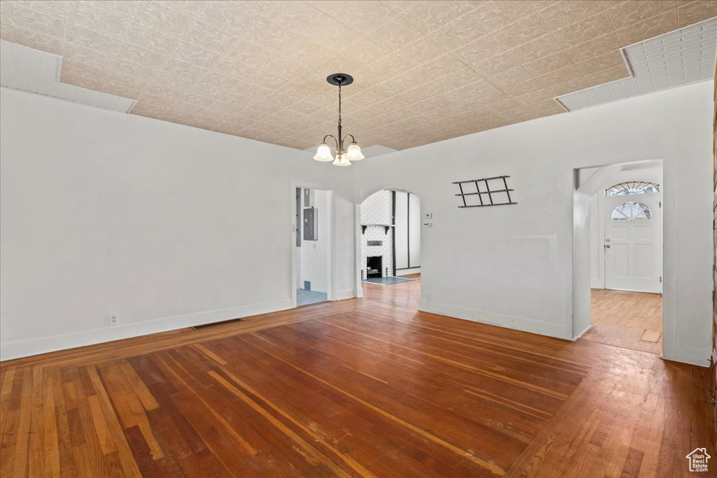 Unfurnished dining area featuring hardwood / wood-style flooring, electric panel, a chandelier, and a brick fireplace