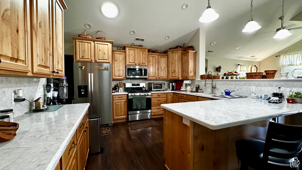 Kitchen featuring lofted ceiling, stainless steel appliances, a kitchen breakfast bar, decorative backsplash, and decorative light fixtures