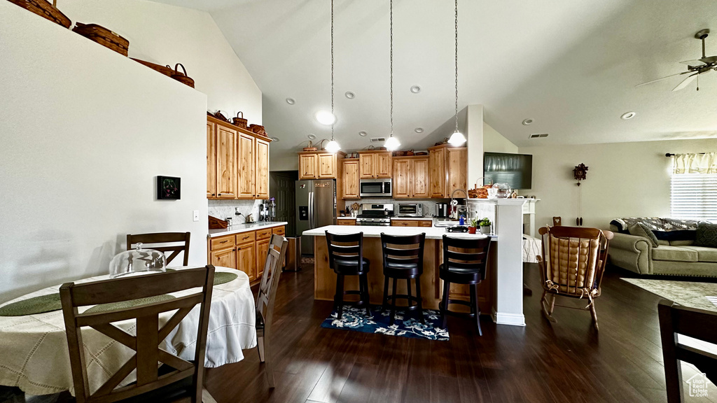 Kitchen with backsplash, stainless steel appliances, dark hardwood / wood-style floors, a kitchen breakfast bar, and decorative light fixtures