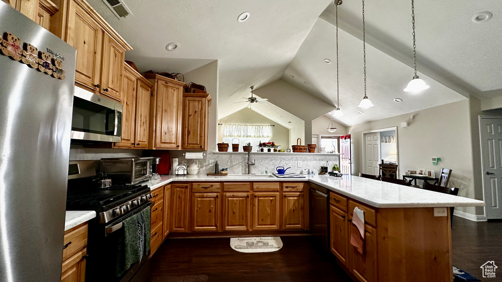 Kitchen featuring vaulted ceiling, appliances with stainless steel finishes, kitchen peninsula, pendant lighting, and decorative backsplash