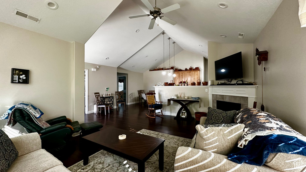 Living room featuring a tile fireplace, wood-type flooring, vaulted ceiling, and ceiling fan