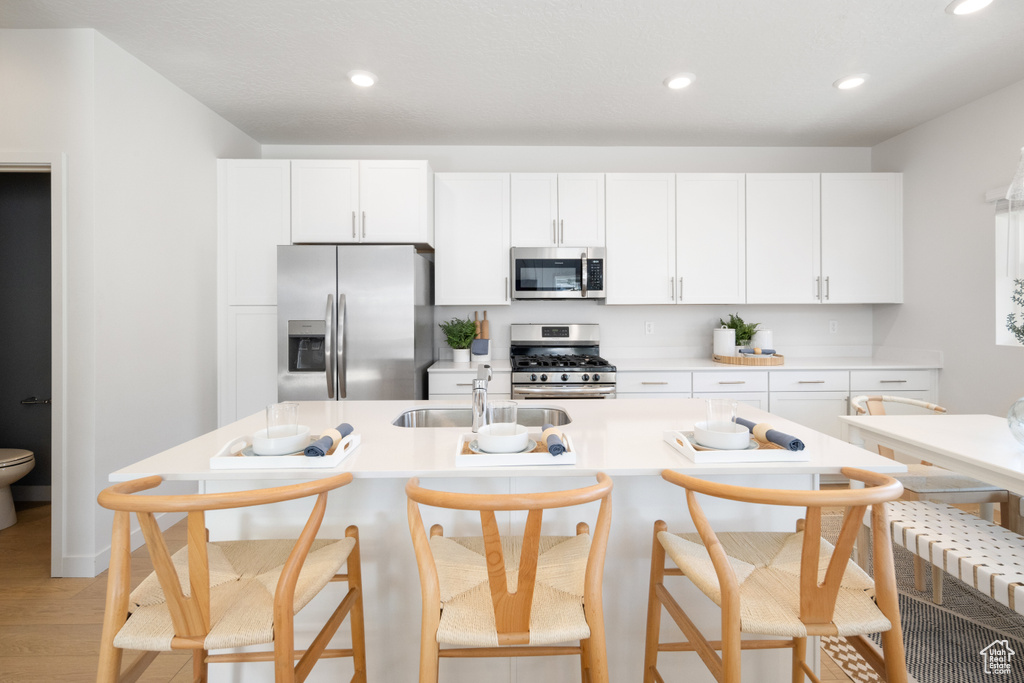 Kitchen with sink, light hardwood / wood-style flooring, a kitchen island with sink, stainless steel appliances, and white cabinets