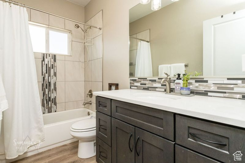 Full bathroom featuring hardwood / wood-style flooring, vanity, tasteful backsplash, shower / bath combination with curtain, and toilet