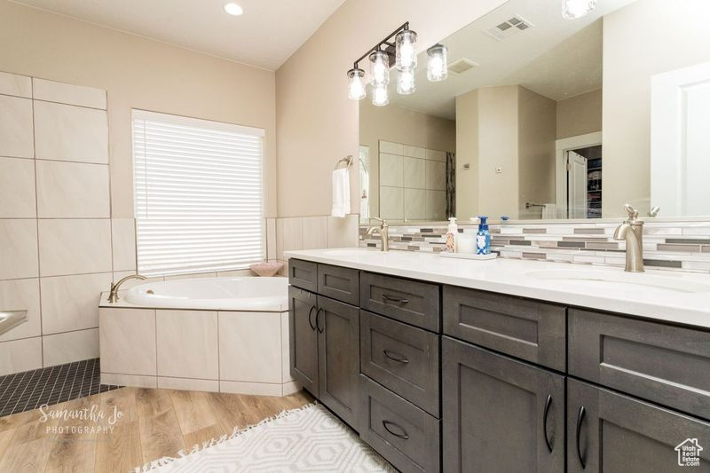 Bathroom featuring wood-type flooring, a tub, tile walls, and vanity