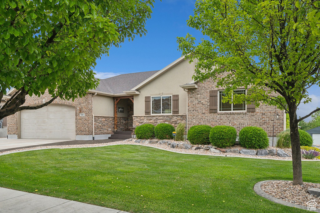 View of front facade with stucco siding, a garage, a front lawn, driveway, and stone siding