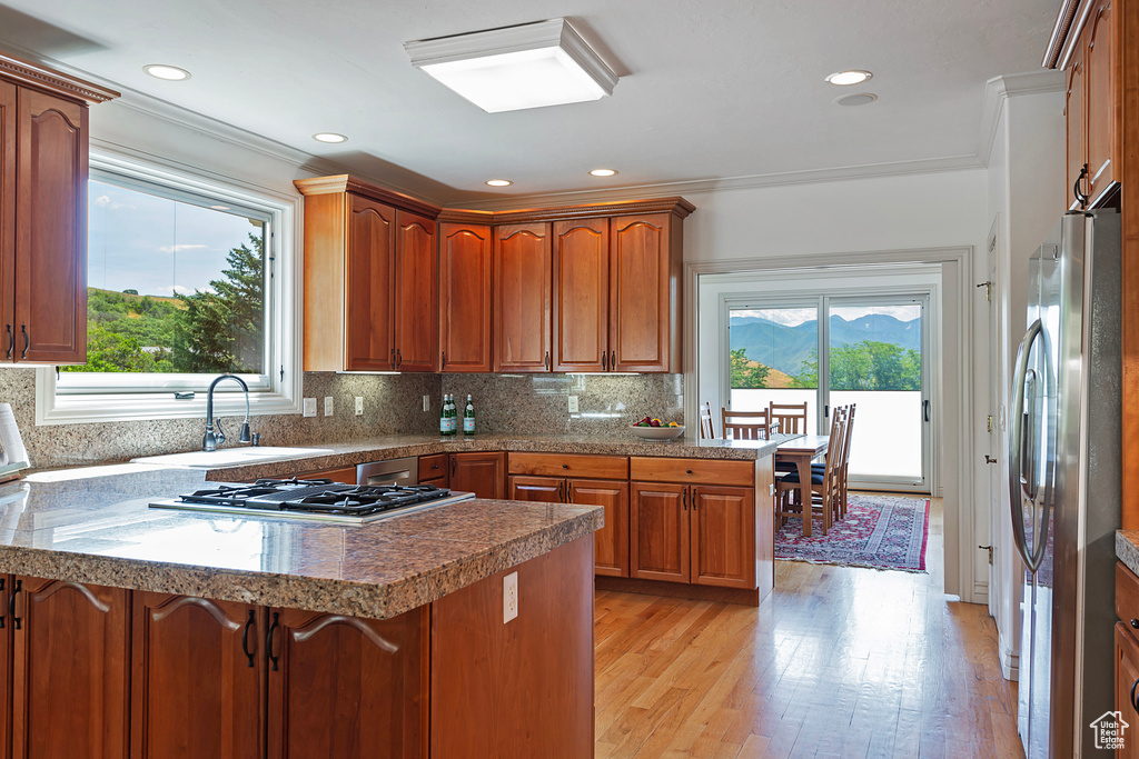 Kitchen with sink, kitchen peninsula, stainless steel appliances, light hardwood / wood-style floors, and decorative backsplash