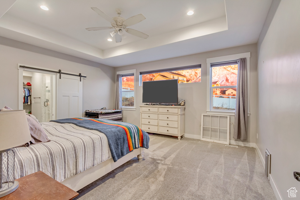 Bedroom featuring ceiling fan, a barn door, a raised ceiling, and light colored carpet