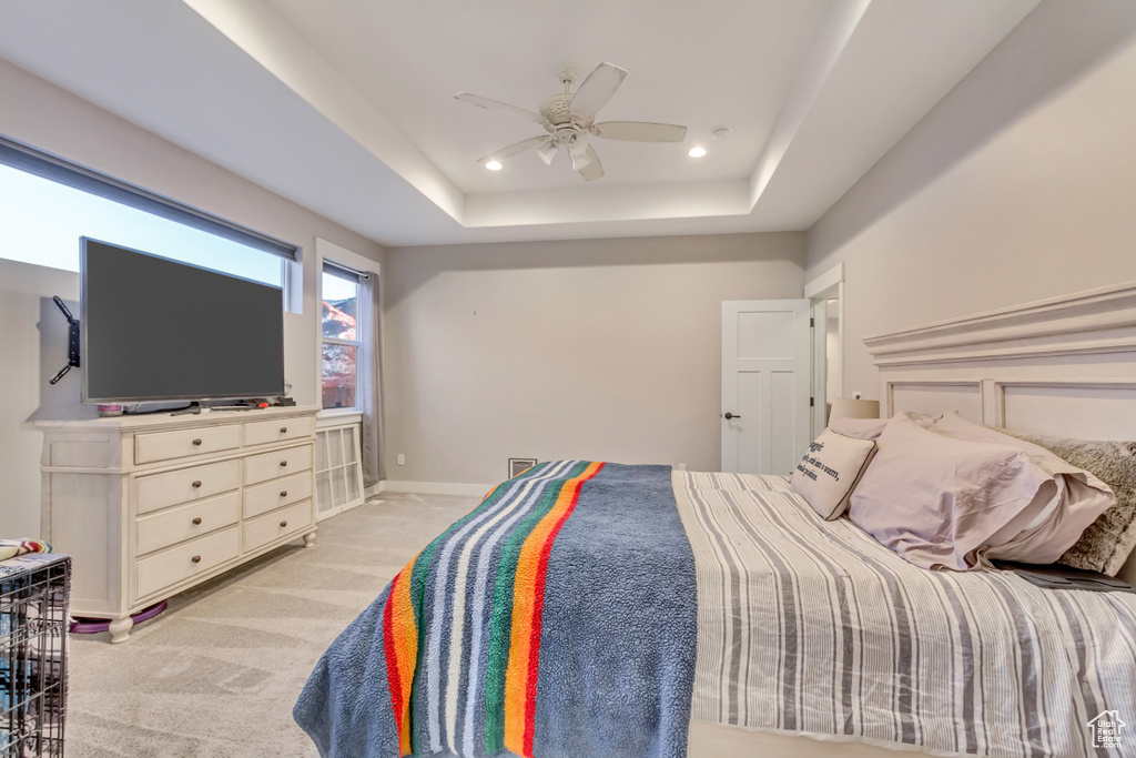 Carpeted bedroom featuring ceiling fan and a tray ceiling