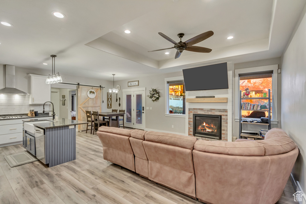 Living room with a raised ceiling, a barn door, sink, and light hardwood / wood-style flooring