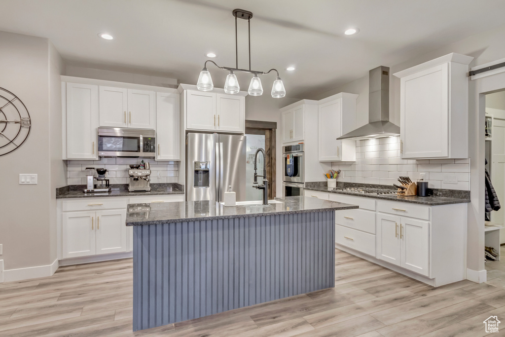 Kitchen featuring white cabinetry, hanging light fixtures, stainless steel appliances, and wall chimney exhaust hood