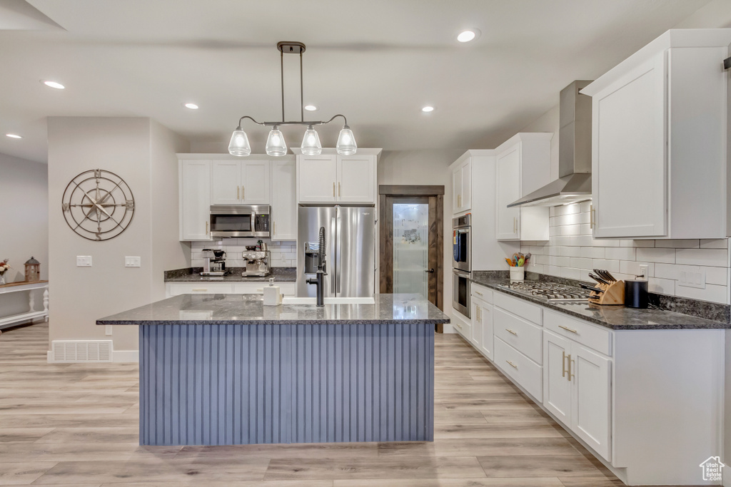Kitchen with white cabinetry, appliances with stainless steel finishes, an island with sink, and wall chimney exhaust hood