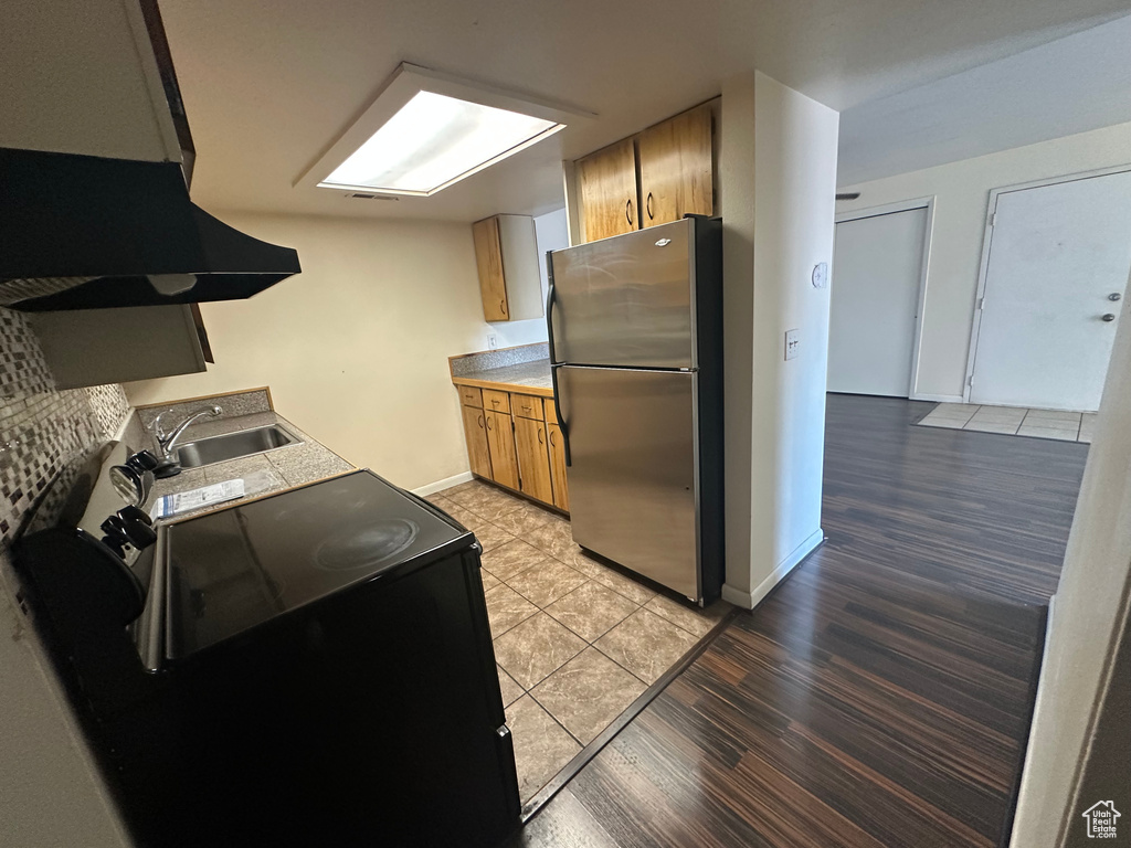 Kitchen with sink, ventilation hood, light wood-type flooring, stainless steel refrigerator, and black range with electric cooktop