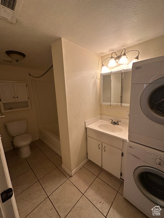 Bathroom with stacked washer / drying machine, tile patterned floors, a textured ceiling, and toilet