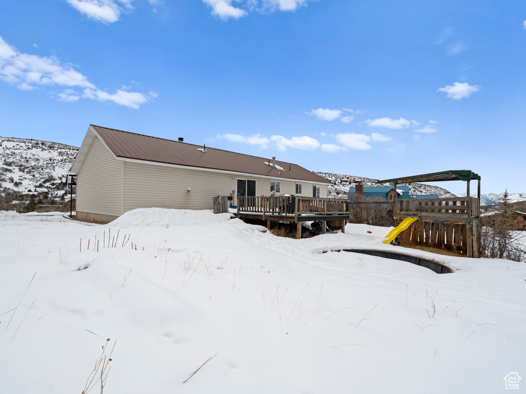 Snow covered house with a playground and a deck