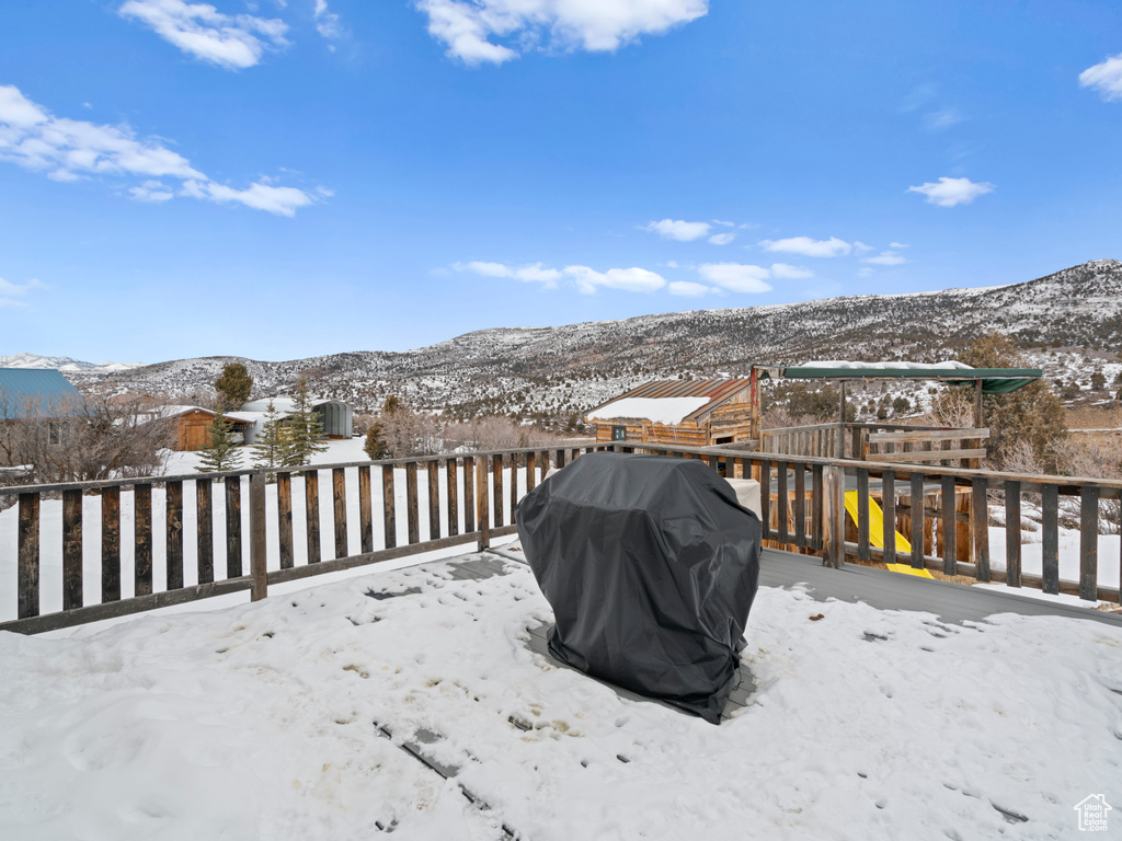 Snow covered deck with a playground, a mountain view, and area for grilling