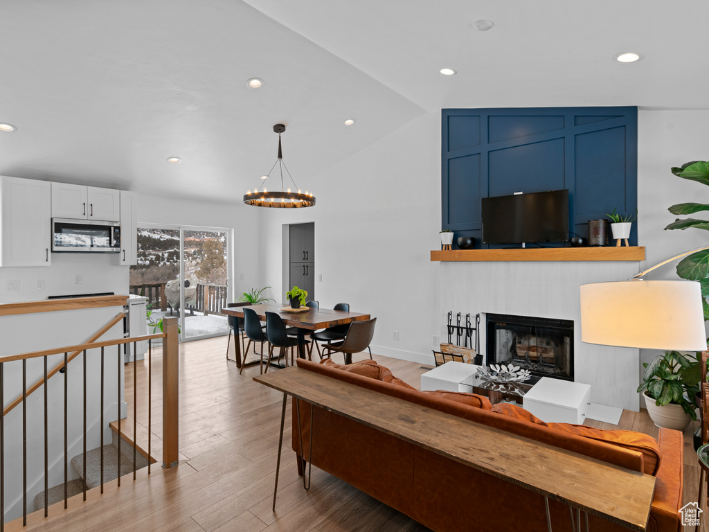 Living room featuring vaulted ceiling, light wood-type flooring, and an inviting chandelier