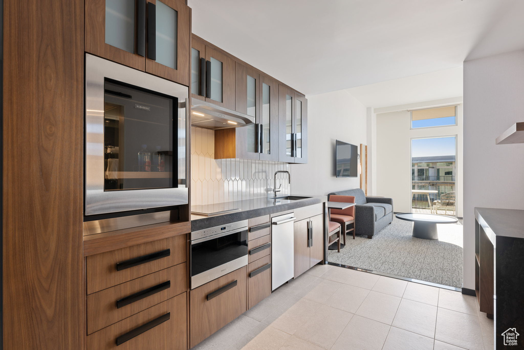 Kitchen with dishwashing machine, black cooktop, sink, wall oven, and light tile patterned floors